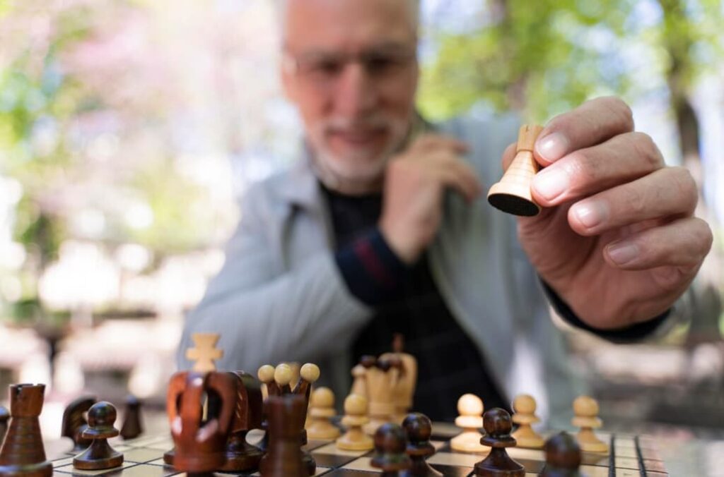 a blurred photo of  man in a gray jacket holds a wooden light figure, the chessboard with figures