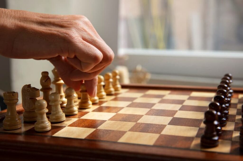 A hand hovers over a chessboard, deciding the next move by daylight