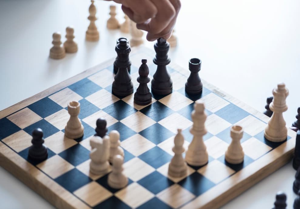 A hand hovers over a chessboard, the chess on the black and white board