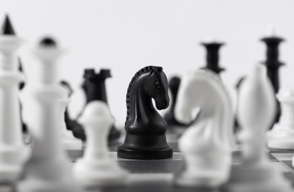 A black chess knight stands in sharp focus amid a blur of surrounding white chess