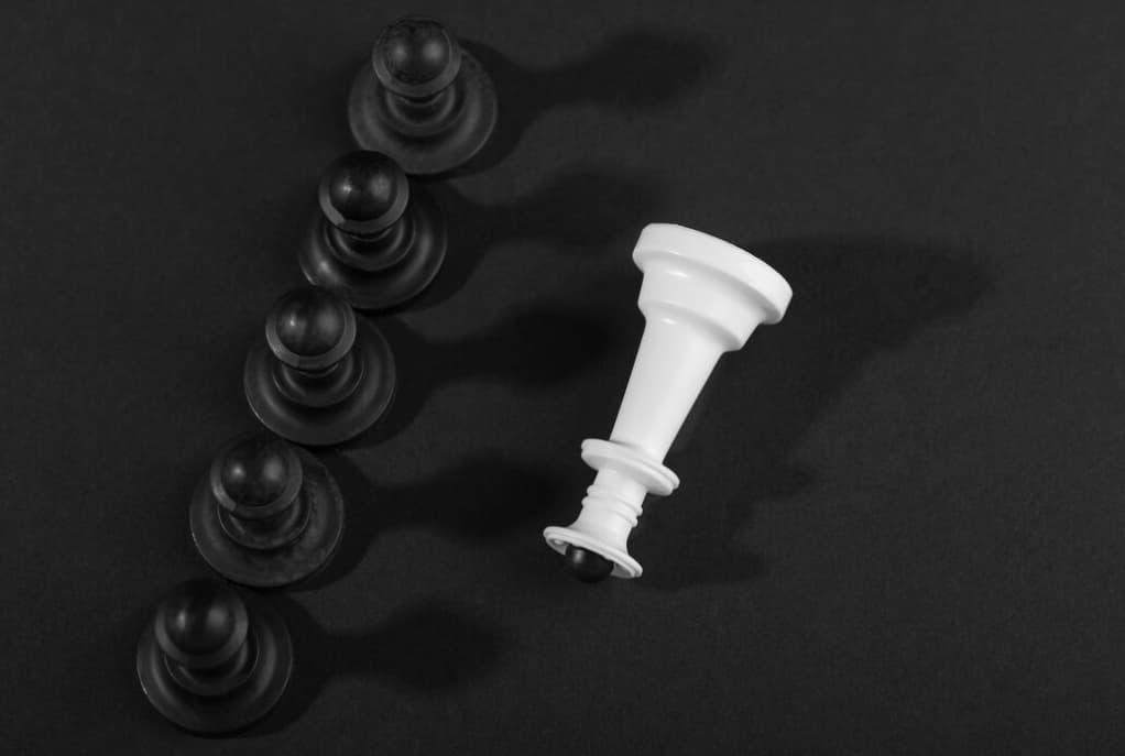 A toppled white chess king lies beside four upright black pawns on a dark background
