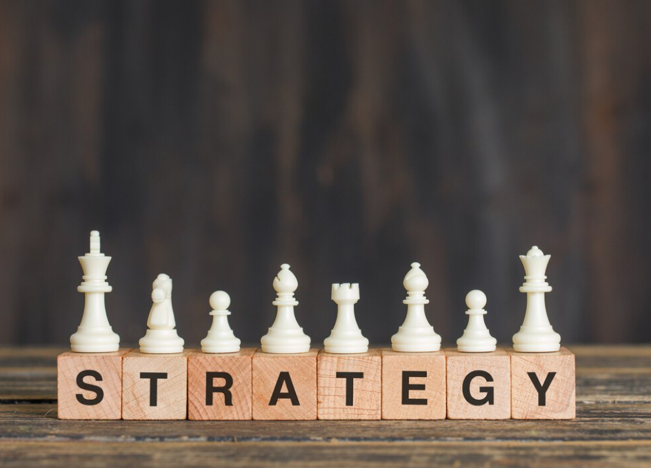 Chess pieces on wooden blocks spelling 'STRATEGY' against a dark wood background